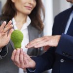 Ein Geschäftsmann und eine Geschäftsfrau in professioneller Kleidung halten gemeinsam eine Glühbirne, die mit grünem Moos bedeckt ist, als Symbol für nachhaltige und umweltfreundliche Innovationen.