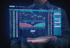 Ein Mann hält eine Hand unter ein schwebendes, transparentes Display mit Kryptowährungs- und Finanzmarktdiagrammen – symbolisch für digitale Finanztechnologie und moderne Datenanalyse.