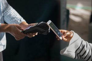 Eine Person hält ein Smartphone über ein Kartenlesegerät und führt eine kontaktlose Zahlung per NFC-Technologie durch – symbolisch für modernes, bargeldloses Bezahlen.