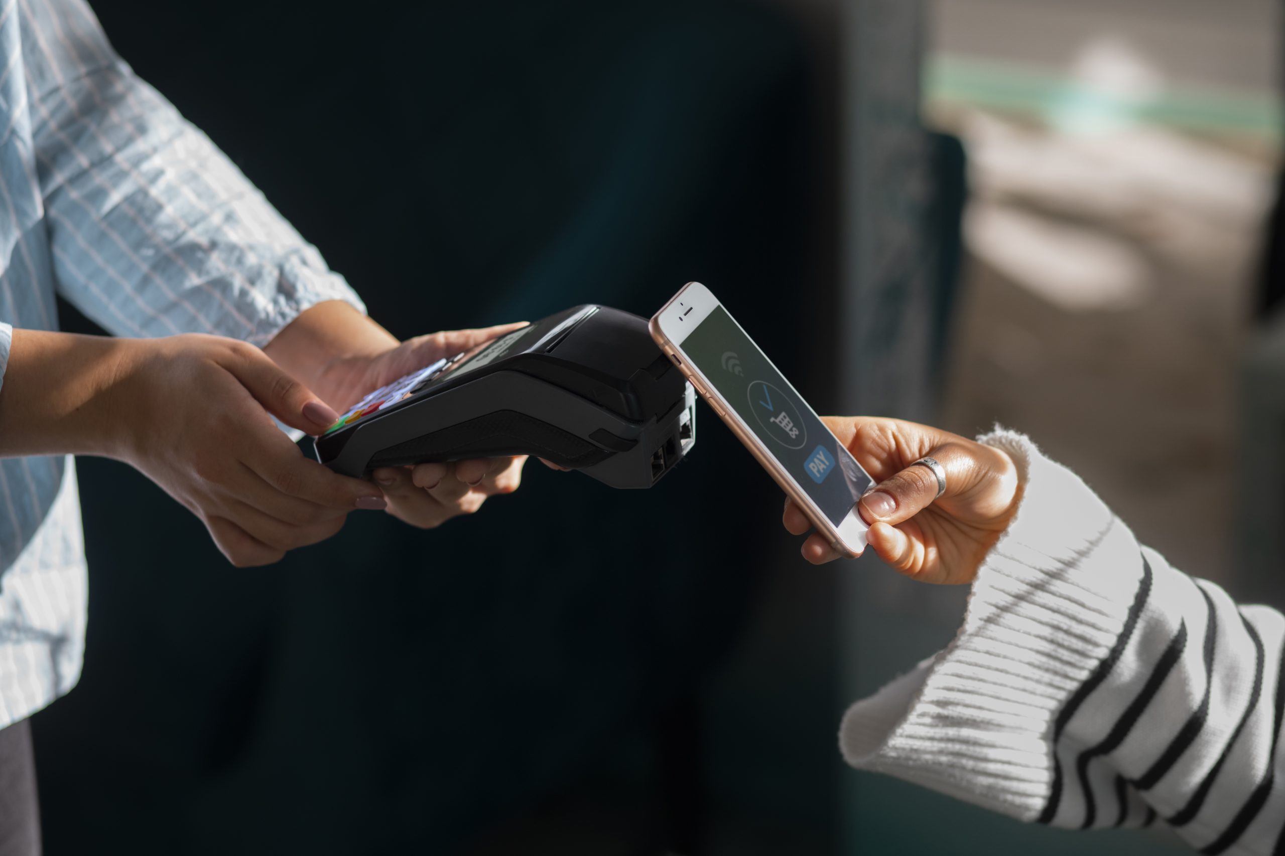 Eine Person hält ein Smartphone über ein Kartenlesegerät und führt eine kontaktlose Zahlung per NFC-Technologie durch – symbolisch für modernes, bargeldloses Bezahlen.
