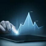 Eine Hand berührt den Bildschirm eines Tablets, auf dem ein leuchtendes, digitales Diagramm mit schwankenden Kurven dargestellt ist, das finanzielle Entwicklungen symbolisiert. Die Szene steht exemplarisch für die Analyse und Überwachung von Investitionen in deutsche Staatsanleihen, die als sichere Anlageoption in einem volatilen Finanzumfeld gelten.