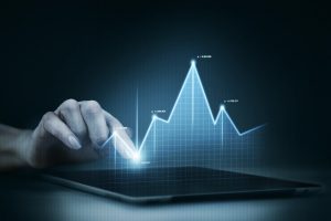 Eine Hand berührt den Bildschirm eines Tablets, auf dem ein leuchtendes, digitales Diagramm mit schwankenden Kurven dargestellt ist, das finanzielle Entwicklungen symbolisiert. Die Szene steht exemplarisch für die Analyse und Überwachung von Investitionen in deutsche Staatsanleihen, die als sichere Anlageoption in einem volatilen Finanzumfeld gelten.