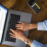 Eine Person tippt auf einem Laptop, während auf dem Bildschirm eine E-Mail-Anwendung geöffnet ist und daneben ein Smartphone mit geöffneter Taschenrechner-App liegt. Die Szene verdeutlicht den Einfluss der Digitalisierung auf die Steuererklärung, da moderne Technologien zunehmend eine effiziente und papierlose Abwicklung steuerlicher Angelegenheiten ermöglichen.