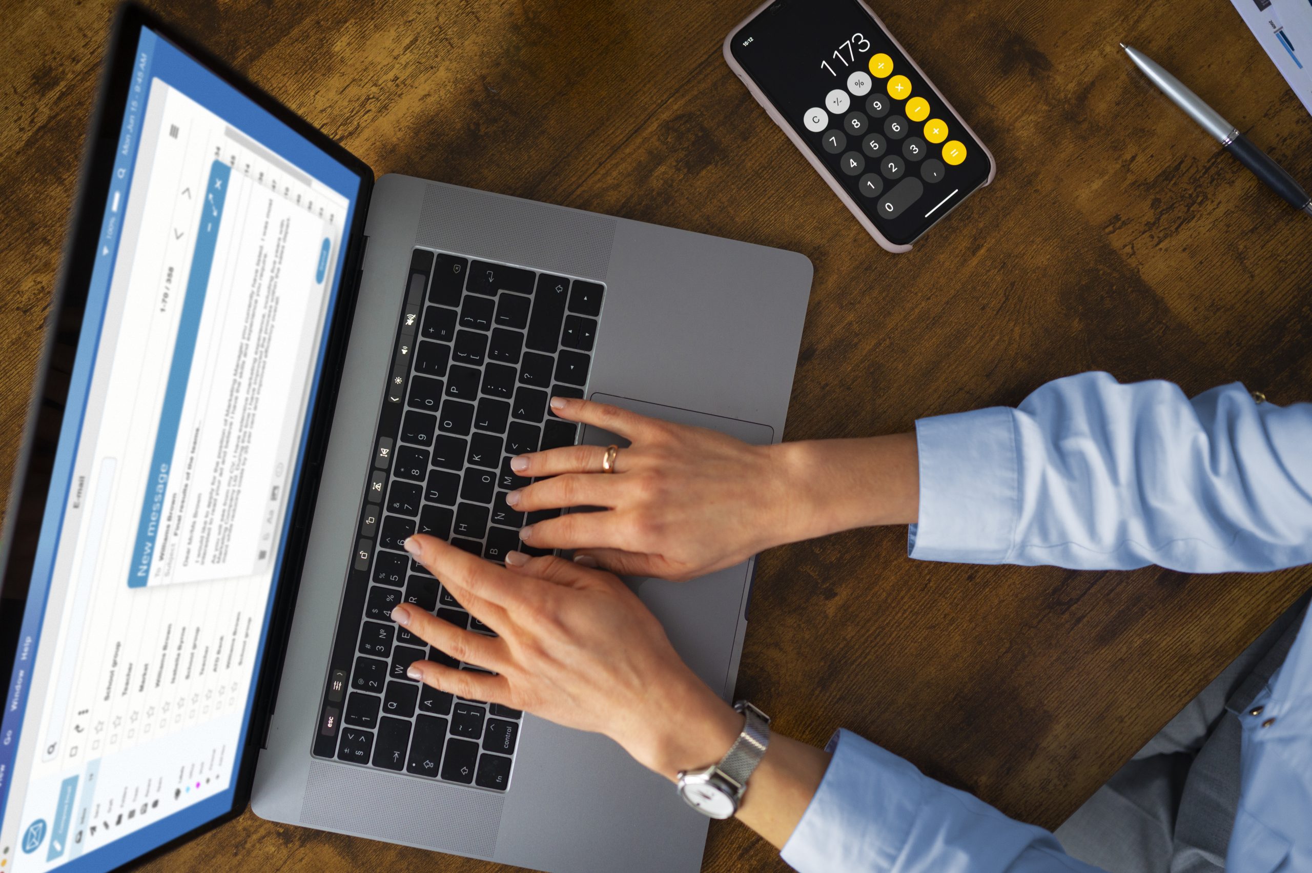Eine Person tippt auf einem Laptop, während auf dem Bildschirm eine E-Mail-Anwendung geöffnet ist und daneben ein Smartphone mit geöffneter Taschenrechner-App liegt. Die Szene verdeutlicht den Einfluss der Digitalisierung auf die Steuererklärung, da moderne Technologien zunehmend eine effiziente und papierlose Abwicklung steuerlicher Angelegenheiten ermöglichen.