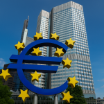 Vor dem modernen Hochhaus des Europäischen Zentralbanksitzes in Frankfurt steht das große blaue Euro-Symbol, umgeben von gelben Sternen der Europäischen Union. Die Szene symbolisiert die wirtschaftliche Stabilität und Herausforderungen wie die Inflation in der Eurozone, die durch geldpolitische Maßnahmen der EZB beeinflusst werden.
