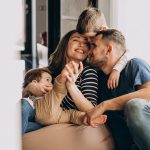 Glückliche junge Familie mit zwei Kindern kuschelt lachend auf dem Sofa – warmes Symbol für Geborgenheit und Schutz durch eine Lebensversicherung.