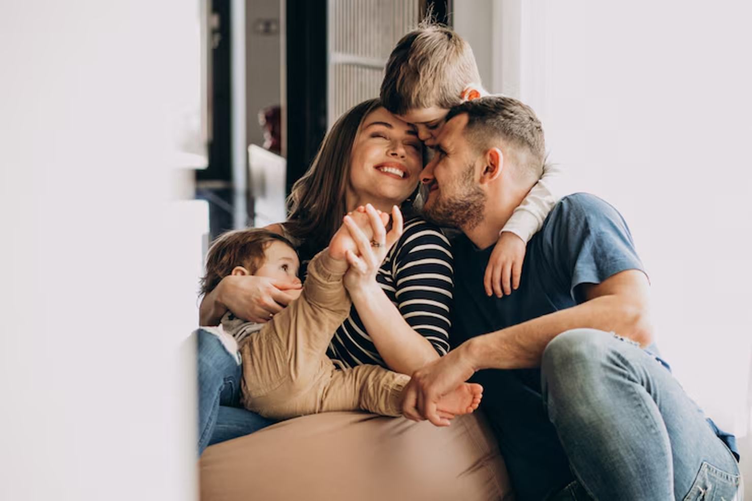 Glückliche junge Familie mit zwei Kindern kuschelt lachend auf dem Sofa – warmes Symbol für Geborgenheit und Schutz durch eine Lebensversicherung.