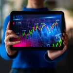 Eine Person hält ein Tablet mit einer farbigen Finanzgrafik, die Kursbewegungen und Zahlen darstellt – symbolische Darstellung der Analyse und Überwachung des deutschen Aktienmarkts in Echtzeit.