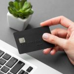Eine Hand hält eine schwarze Kreditkarte über der Tastatur eines Laptops, bereit für eine Online-Transaktion. Die Szene symbolisiert modernes digitales Einkaufen und die Bedeutung von Kreditlimits bei der Verwaltung persönlicher Finanzen.