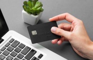 Eine Hand hält eine schwarze Kreditkarte über der Tastatur eines Laptops, bereit für eine Online-Transaktion. Die Szene symbolisiert modernes digitales Einkaufen und die Bedeutung von Kreditlimits bei der Verwaltung persönlicher Finanzen.