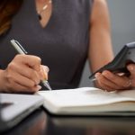 Frau berechnet Finanzen mit Notizbuch und Taschenrechner am Schreibtisch, Symbol für Planung und Verwaltung der Sozialversicherung.