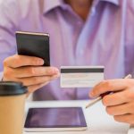 Mann hält eine Kreditkarte und ein Smartphone in der Hand, Symbol für Online-Zahlungen und dafür, wie man unberechtigte Kreditkartenabrechnungen in Deutschland beanstandet.