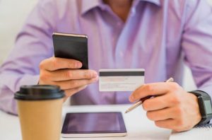 Mann hält eine Kreditkarte und ein Smartphone in der Hand, Symbol für Online-Zahlungen und dafür, wie man unberechtigte Kreditkartenabrechnungen in Deutschland beanstandet.