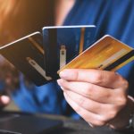 Eine Person hält drei Co-Branded-Kreditkarten in der Hand, während sie mit der anderen Hand auf einem Laptop tippt – ein Symbol für Online-Einkäufe und die Nutzung partnerschaftlicher Kreditkartenangebote.