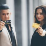 Mann und Frau halten jeweils eine Kreditkarte in der Hand, Symbol für den Einsatz von revolvierenden und Ratenkreditkarten im modernen Finanzwesen.