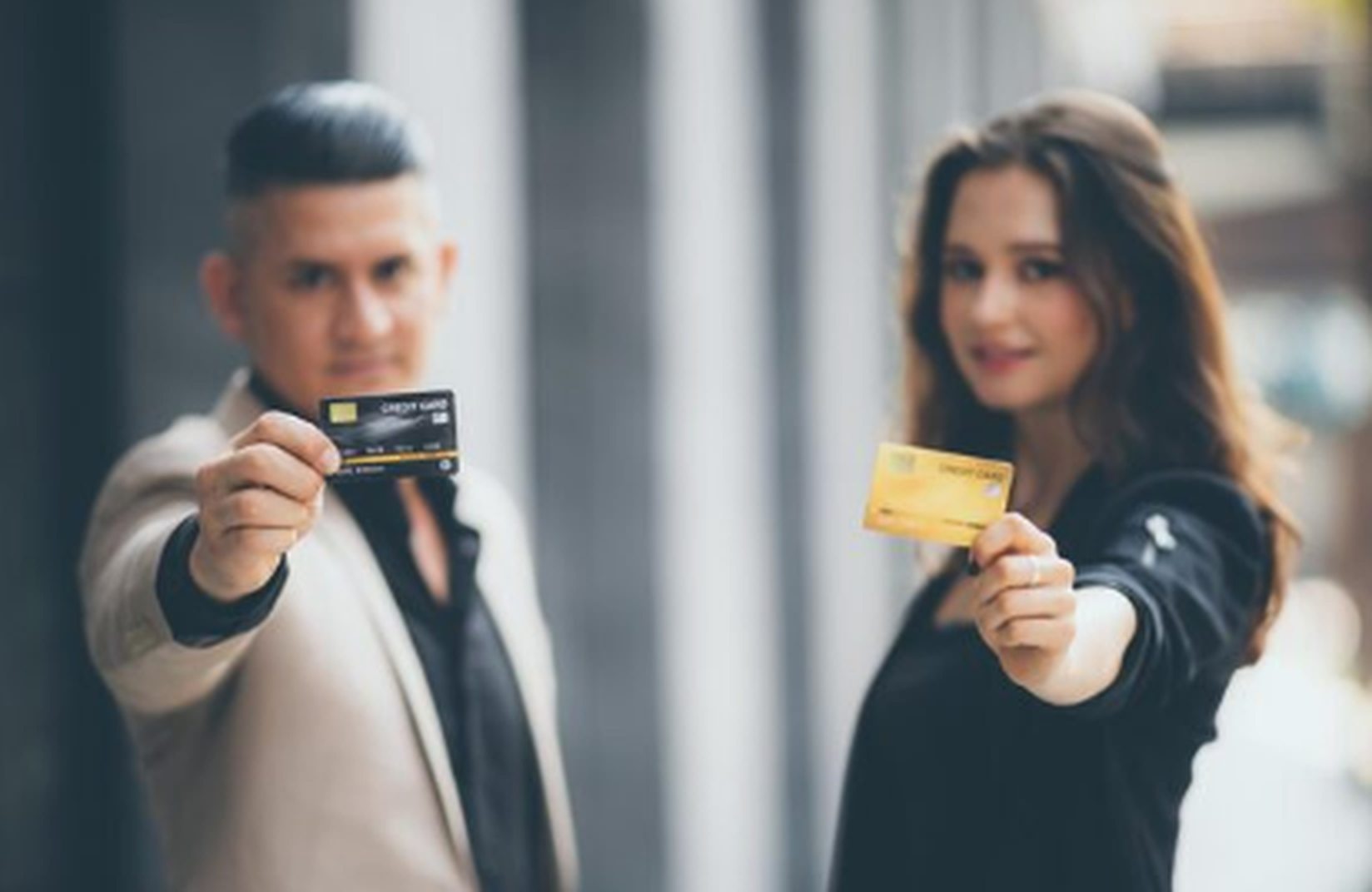 Mann und Frau halten jeweils eine Kreditkarte in der Hand, Symbol für den Einsatz von revolvierenden und Ratenkreditkarten im modernen Finanzwesen.