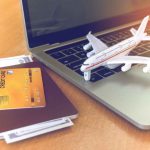 Reisepass mit Kreditkarte und Bargeld neben einem Laptop, daneben ein Modellflugzeug – Symbol für Reisen und Vorteile durch Kreditkarten-Meilenprogramme.