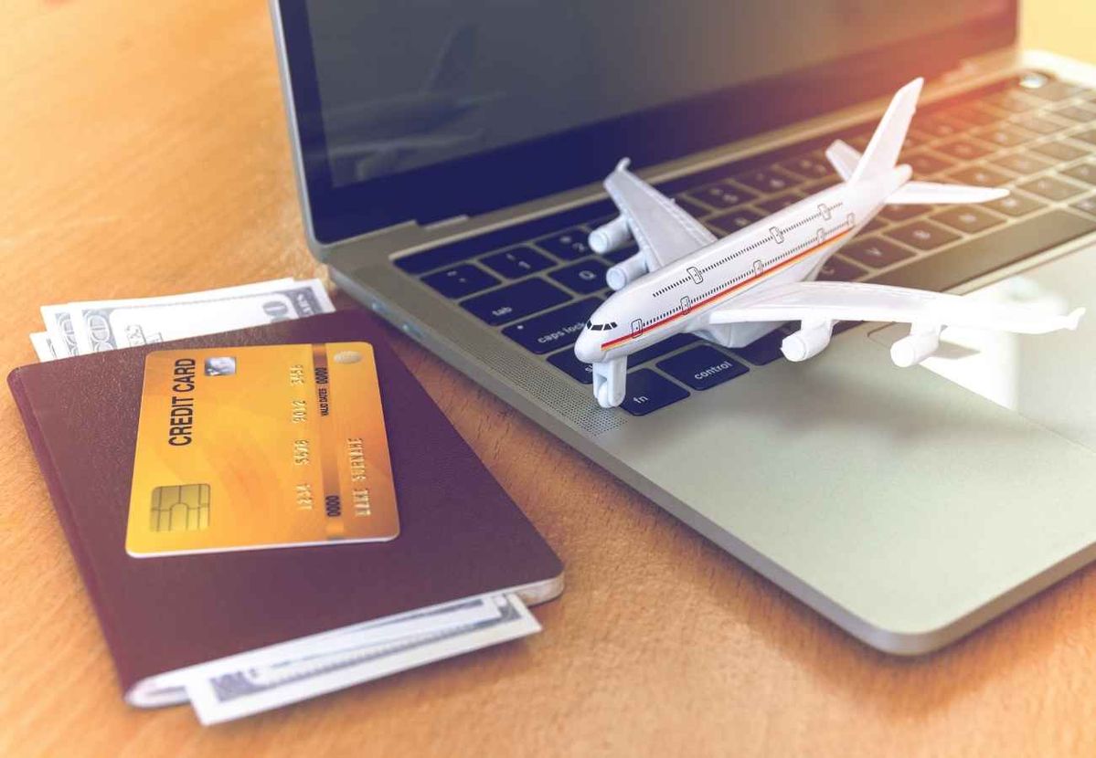 Reisepass mit Kreditkarte und Bargeld neben einem Laptop, daneben ein Modellflugzeug – Symbol für Reisen und Vorteile durch Kreditkarten-Meilenprogramme.