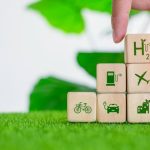 Holzwürfel mit Symbolen für Fahrrad, Elektroauto, Wasserstoff, Flugzeug und nachhaltige Gebäude auf grüner Wiese – eine Darstellung von Innovation und Nachhaltigkeit in der Mobilität und Energieversorgung.