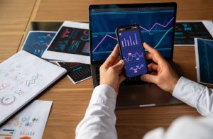 Person analysiert Finanzdiagramme auf Laptop und Smartphone, um Investitionsstrategien mit Hilfe von digitalen Werkzeugen besser zu planen und zu überwachen.