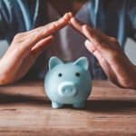 Person, die ihre Hände schützend über ein blaues Sparschwein hält, symbolisiert den Schutz von Ersparnissen und finanzieller Stabilität während einer Rezession.