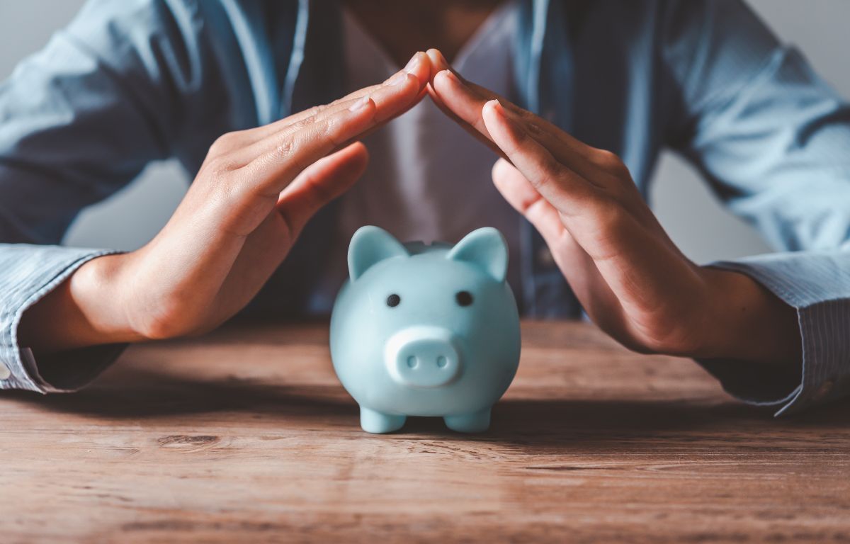 Person, die ihre Hände schützend über ein blaues Sparschwein hält, symbolisiert den Schutz von Ersparnissen und finanzieller Stabilität während einer Rezession.